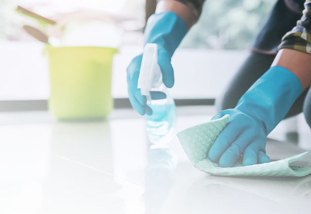 Hands in reusable gloves cleaning the floor with a spray bottle and cloth, representing Nixxie Trades Sense Cleaning & Chemical Disinfection products.