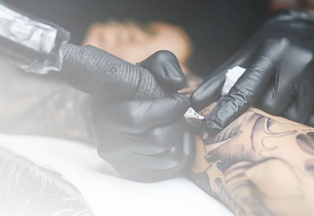 Hands wearing black disposable gloves creating a tattoo, representing Nixxie Trades Sense Tattoo Shop Supplies.