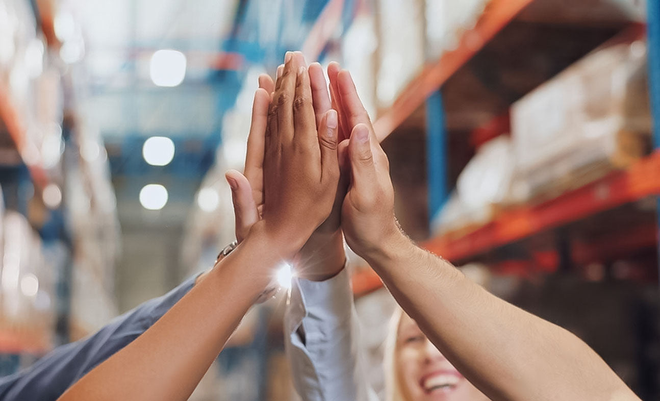 Team high-fiving in a warehouse, representing Nixxie Trades Sense's commitment to premium wholesale and retail solutions.